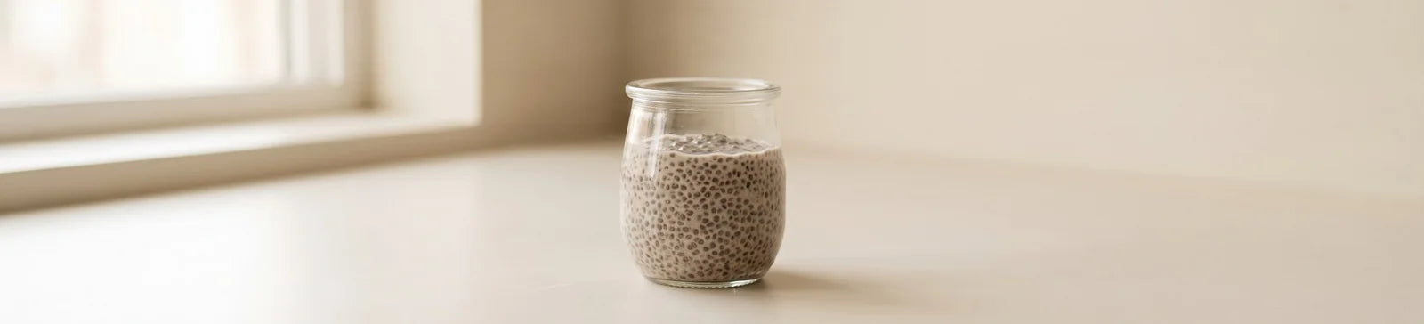 A glass jar of chia protein pudding on a light counter by a window