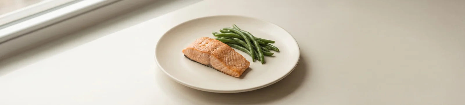 A roasted salmon fillet with green beans on a white plate