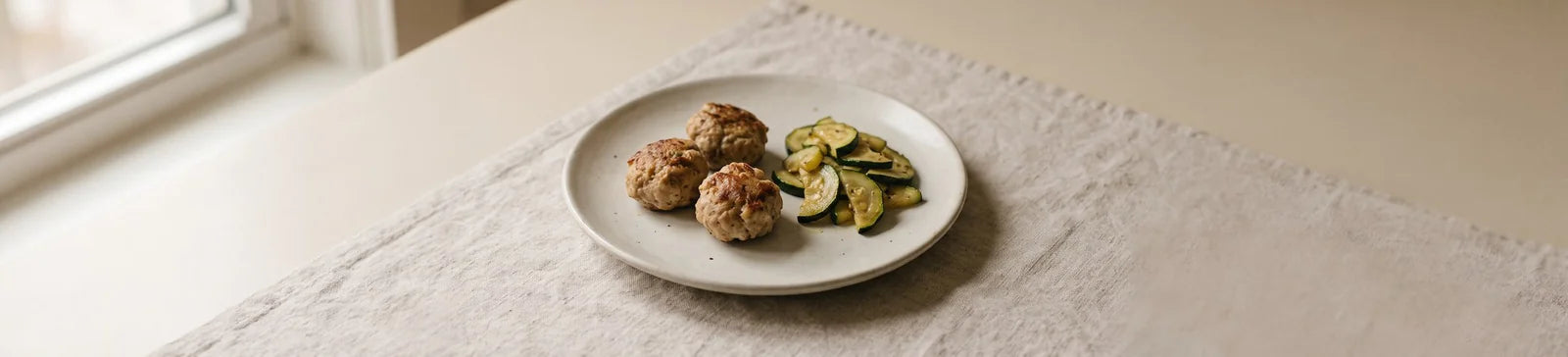 Three turkey meatballs next to sauteed zucchini slices on a plate