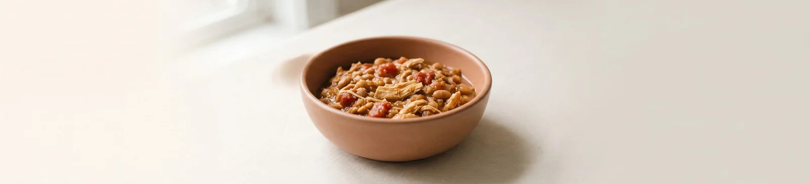A terracotta bowl of chicken chili with beans and tomatoes