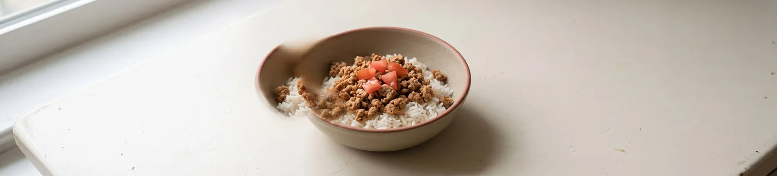 A bowl of seasoned ground turkey over white rice topped with diced tomato