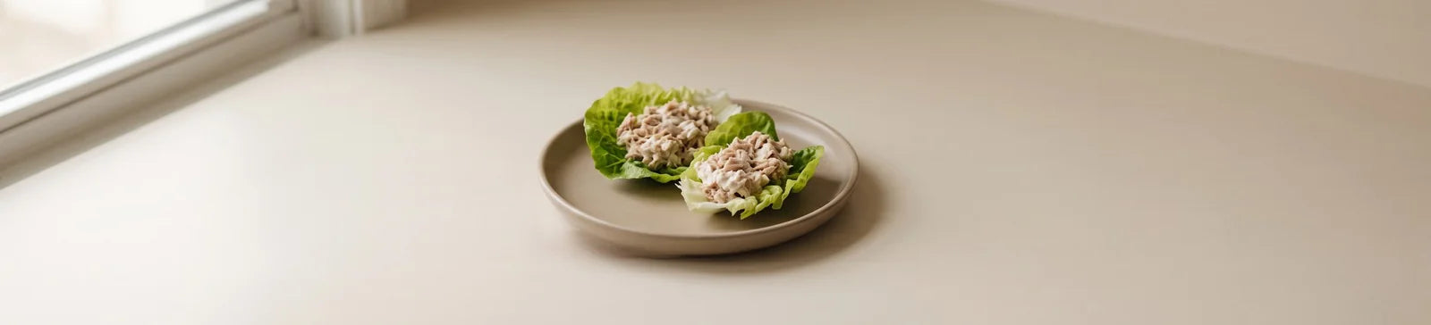 Two lettuce cups filled with tuna salad on a small plate