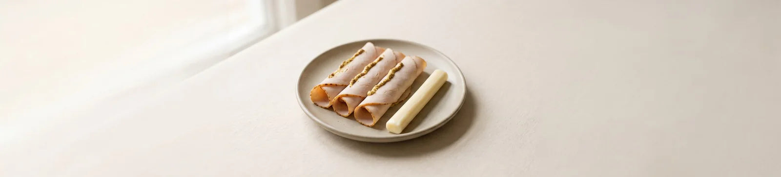 Three rolled slices of deli turkey next to a stick of string cheese on a plate