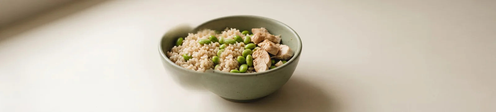 A green bowl of cooked grain topped with edamame and diced chicken