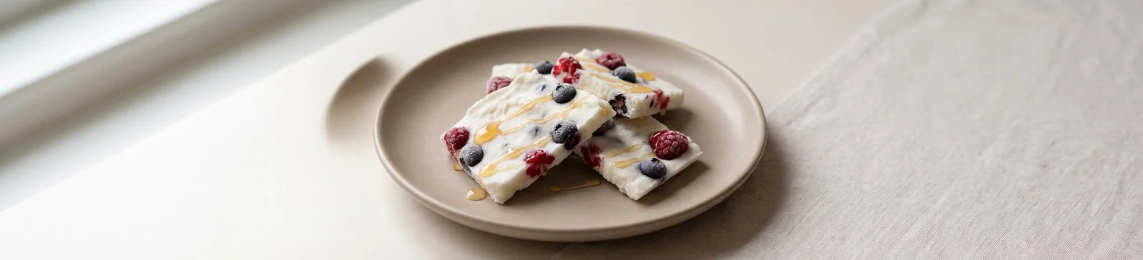 Pieces of frozen Greek yogurt bark with raspberries, blueberries and a honey drizzle on a beige plate