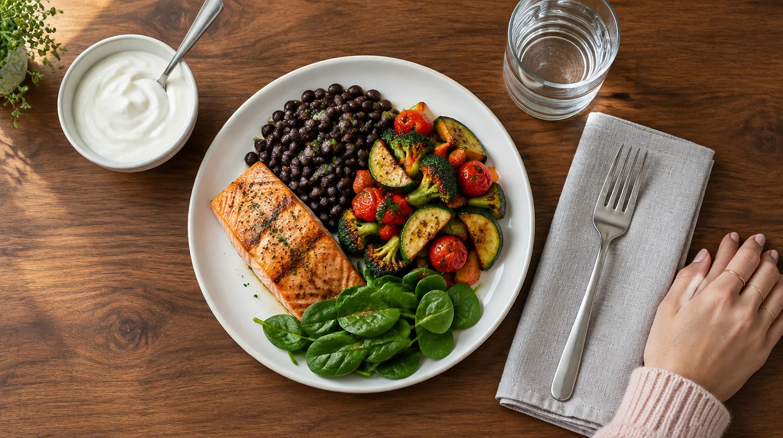 Overhead view of a plate with grilled salmon, black beans, roasted vegetables, and spinach, next to a bowl of Greek yogurt and a glass of water